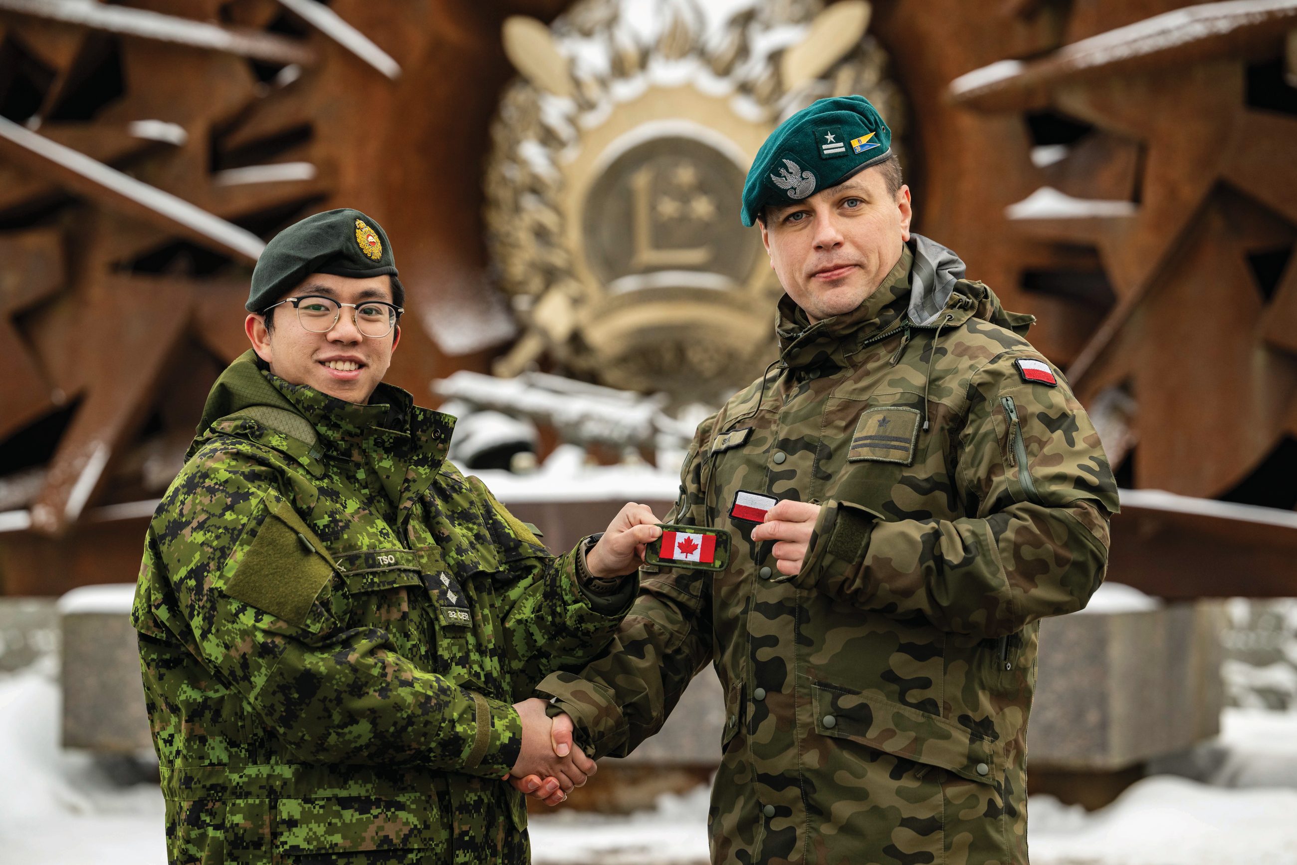 Kanadyjski por. Samson Tso i polski mjr Tomasz Sęk z Batalionowej Grupy Bojowej Wzmocnionej Wysuniętej Obecności NATO na Łotwie, wymieniają się naszywkami z flagami narodowymi przed zakończeniem zmiany w bazie Ādaži na Łotwie, 7 grudnia 2023 rok.